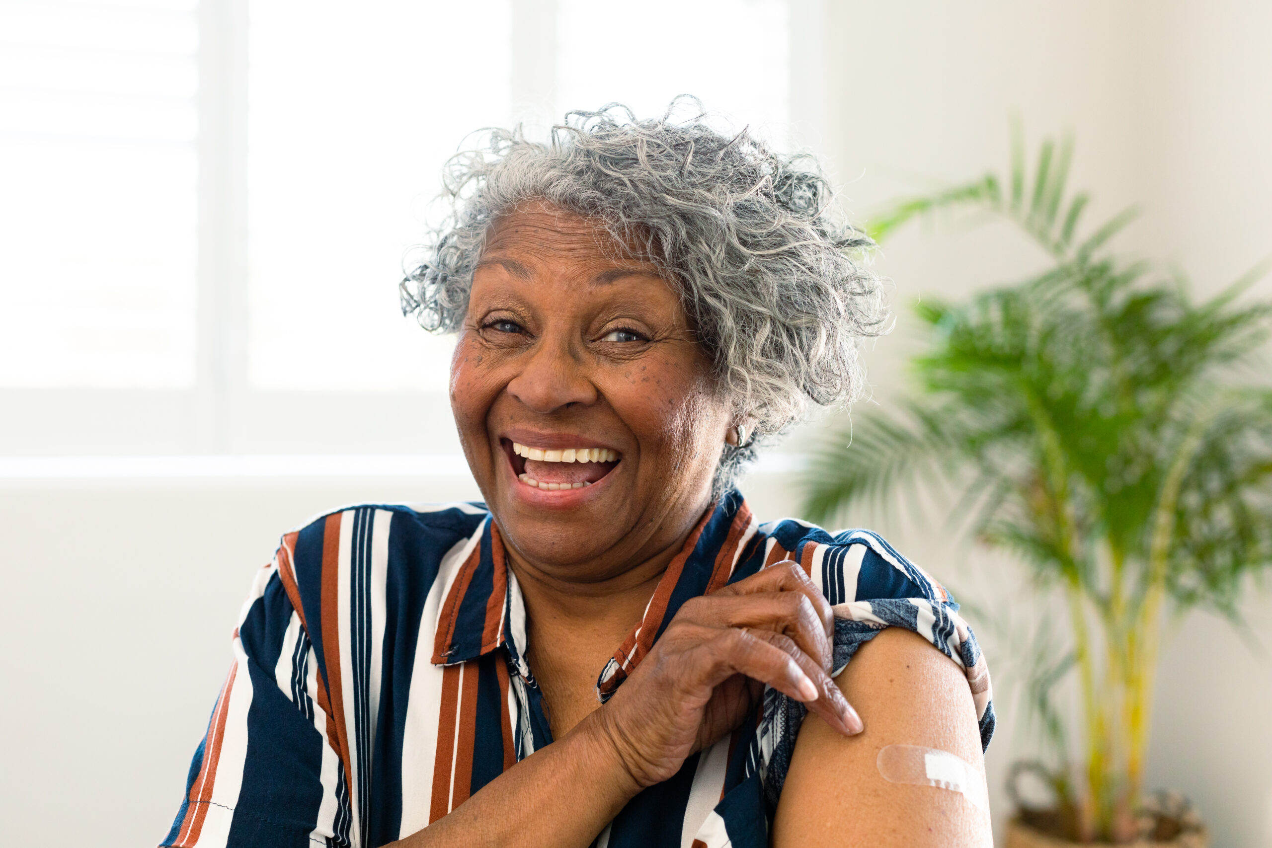 Happy senior african american woman with plaster on arm looking at camera after vaccination. senior health and lifestyle during covid 19 pandemic.